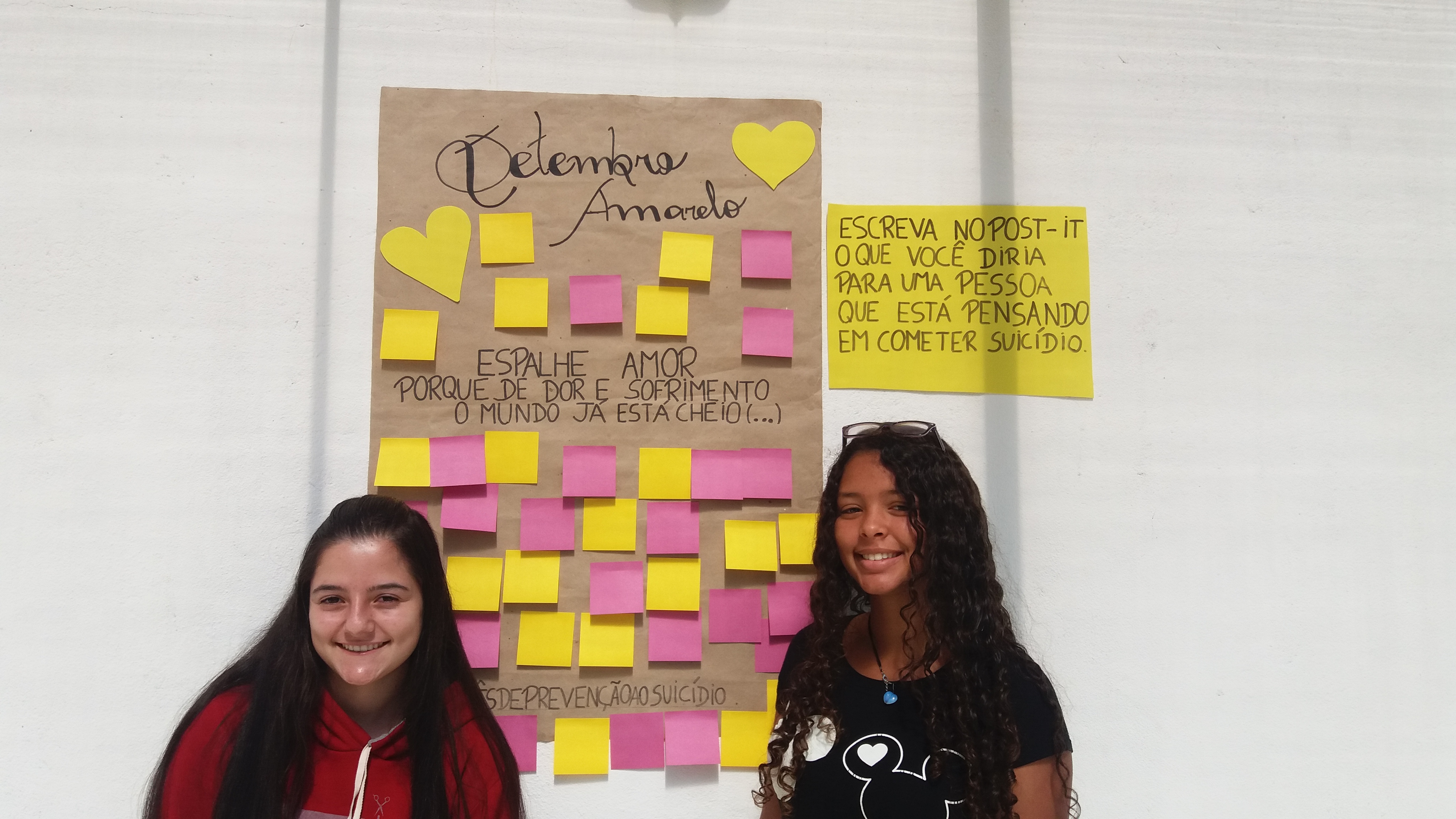 Duas alunas do Campus Avançado Carmo de Minas posam em frente ao cartaz da campanha
